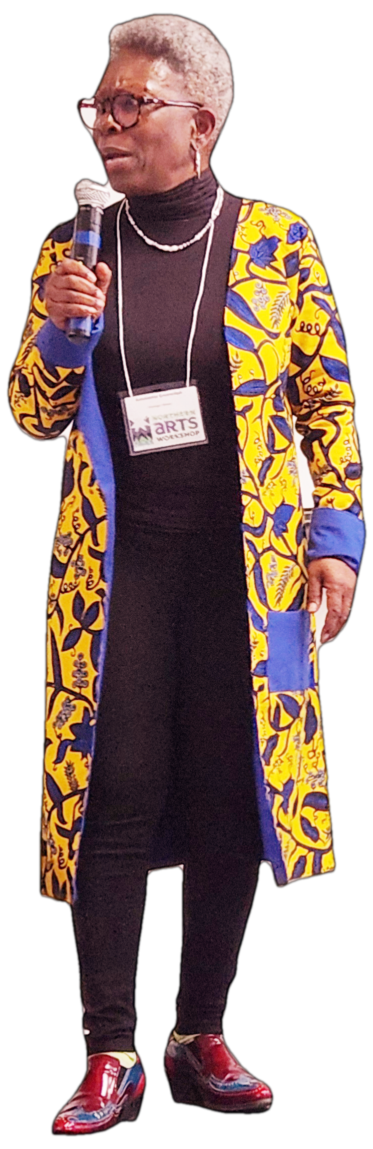 Antoinette GreenOliph, keynote speaker at the Northern Arts and Food Workshop in The Pas, MB on March 25, 2024. Full body photo of black woman, wearing a long yellow and blue patterned jacket with black pants and top and Fluvog red and blue shoes.
